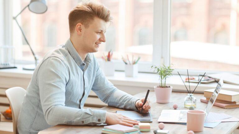 fair skinned young man drawing on tablet and smiling as he looks at his computer