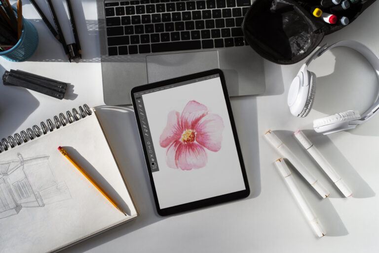 illustration of flower on drawing tablet, arranged near a sketchpad, computer, and headphones